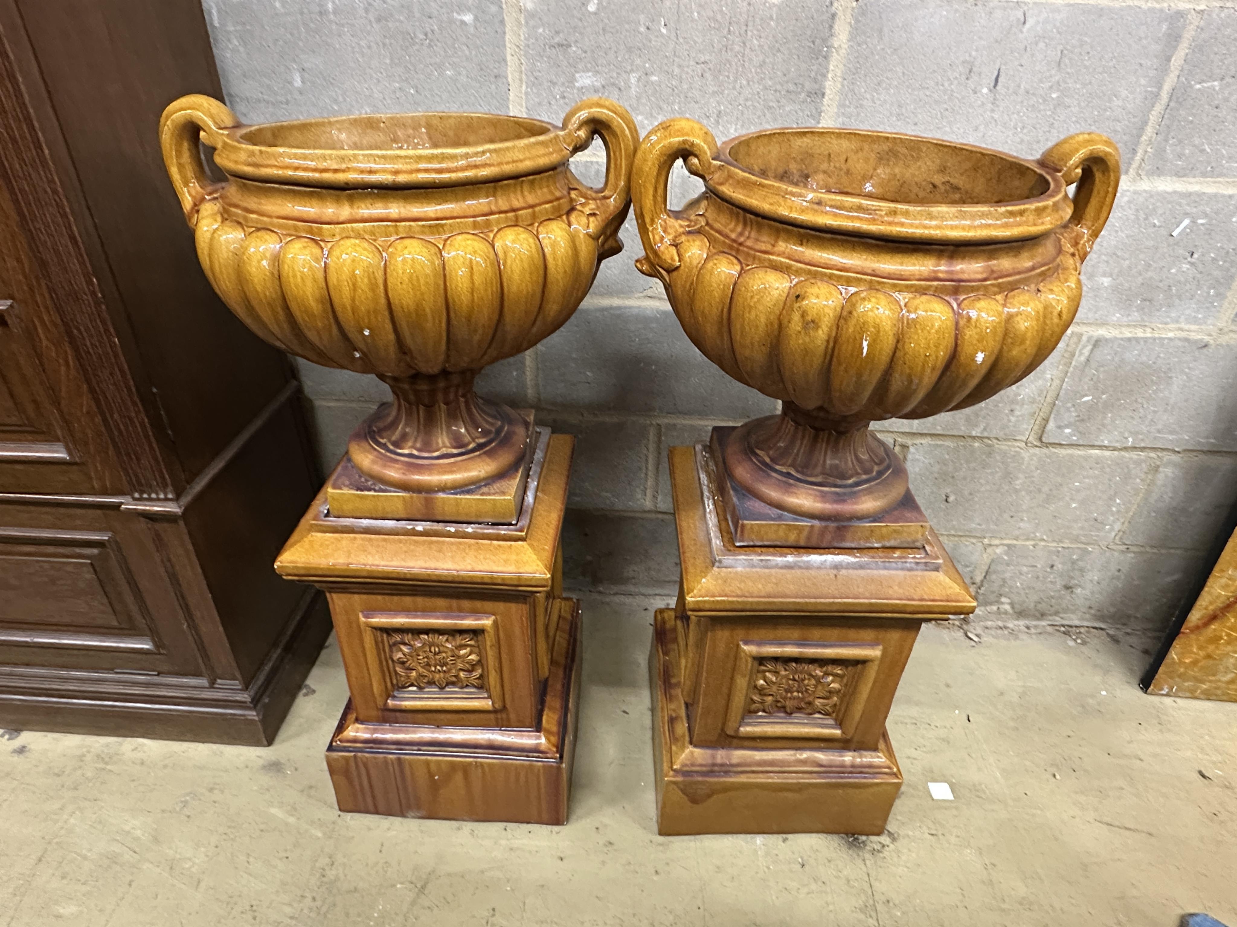 A pair of Victorian treacle glazed earthenware twin handled urns on square stands, height 104cm. Condition - fair, some losses to plinths